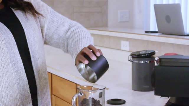 Beautiful Young African-American Woman Grinding Coffee and pouring it into a pour over coffee filter at home