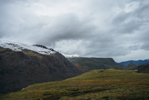 istock Atmospheric alpine landscape with deep gorge and snow-capped multicolor mountains in overcast weather. Beautiful scenery with snowbound mountain range under cloudy sky. Motley high mountains with snow 1353898741