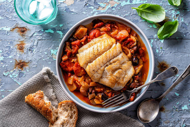 Mediterranean Style Fish A plate of delicious Mediterranean style pan fried fish with tomato, fennel, onion and kalamata olives on a rustic table top. haddock stock pictures, royalty-free photos & images