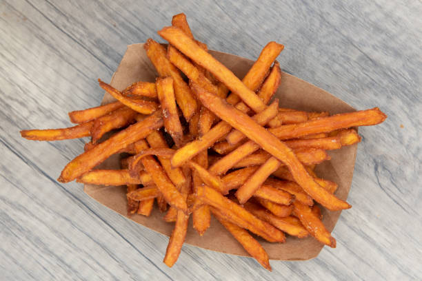 Food straight from the kitchen to your table. Overhead view of crispy side dish of sweet potato french fries served in a cardboard boat to eat on the go. sweet potato french fries stock pictures, royalty-free photos & images