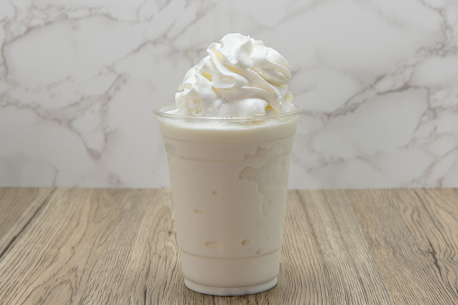 Vanilla milk shake served cold and frosty in a cup and topped with sweet whipped cream.