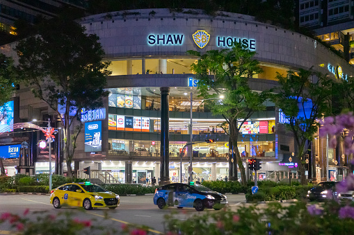 Singapore, Singapore - November 6, 2021: Taxis pass by Shaw House, a shopping mall located on Orchard Road housing department store Isetan, restaurants and a cinema complex.