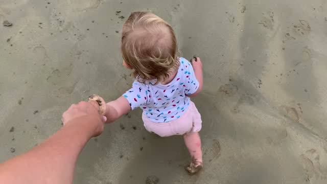 toddler girl walking at the beach holding hands of mother, view from the top