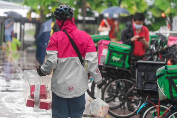 Food delivery workers working on a rainy day in Singapore Singapore, Singapore - November 18, 2021: A Foodpanda delivery worker carrying bags of food walks towards bicycles parked outside the Jurong Point shopping mall on a rainy day. super bike stock pictures, royalty-free photos & images