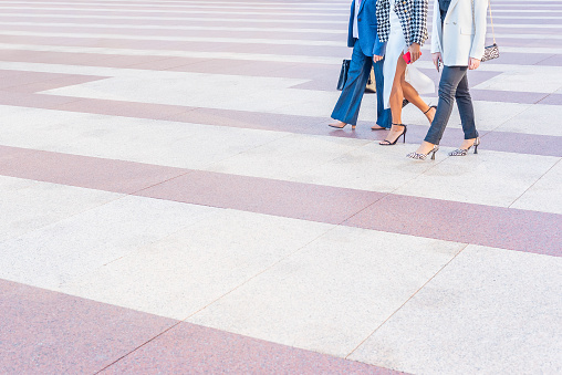 three business women walking across a pedestrian crossing. View of the legs