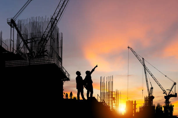 istock Silhouette of Engineer and worker on building site, construction site at sunset in evening time. 1353940810
