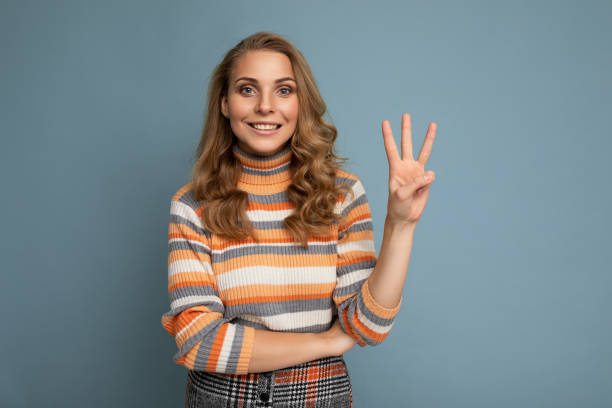 foto einer jungen positiven, glücklich lächelnden schönen frau mit aufrichtigen emotionen, die stilvolle kleidung trägt, die über dem hintergrund mit kopierraum isoliert ist und drei finger zeigt - drei personen stock-fotos und bilder