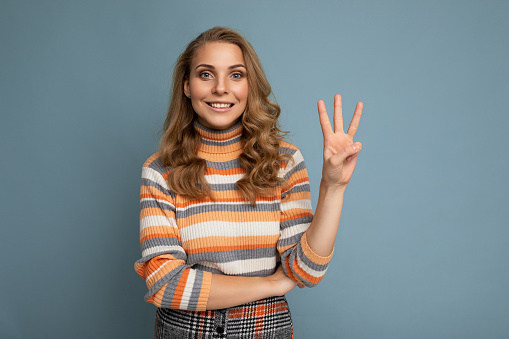 Photo of young positive happy smiling beautiful woman with sincere emotions wearing stylish clothes isolated over background with copy space and showing three fingers.