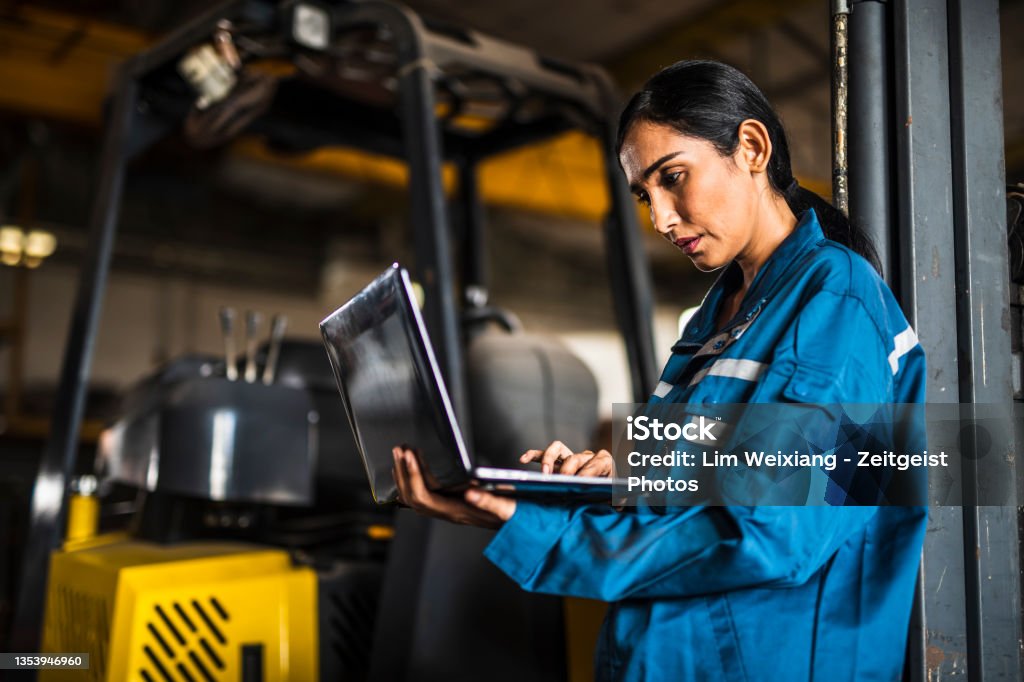 Indian Female Steel Factory Worker using a laptop Indian Female Steel Factory Worker using a laptop in front of forklift Manufacturing Stock Photo