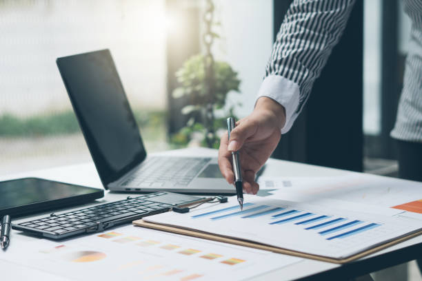 istock Businessman holding pen and pointing paper chart summary analyzing annual business report with using laptop at room office desk. 1353947023