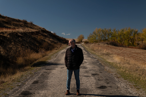 Portrait of adult man in winter cloth on a country road against blue sky. Shot in Castilla y Leon, Spain