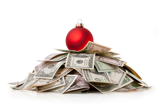 Red Christmas ball standing on a stack of US dollars isolated on white background.