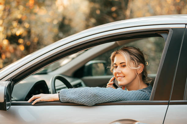 giovane bella donna bionda che parla sullo smartphone apri il finestrino dell'auto mentre ferma il veicolo, sorridendo. felice viaggio gioioso, momento di relax, stile di vita attivo, osservanza delle regole del traffico. - car phone foto e immagini stock