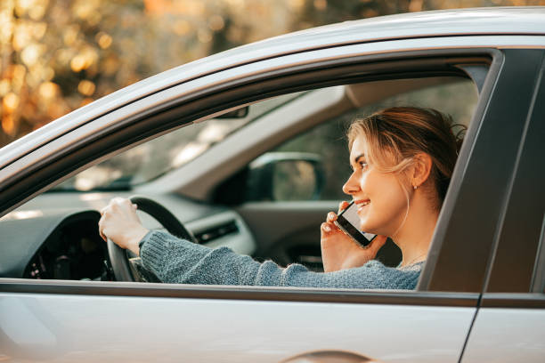 водитель блондинки разговаривает на смартфоне за рулем автомобиля, не внимательно управляя автомобилем, нарушая правила дорожного движен� - car phone стоковые фото и изображения