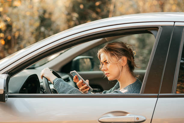 若い美しい女性は、車を運転し、交通ルールに違反し、気を散らし、携帯電話の画面を見て、スマートフォンを使用し、速いペースで現代生活の概念 - car insurance driving women ストックフォトと画像