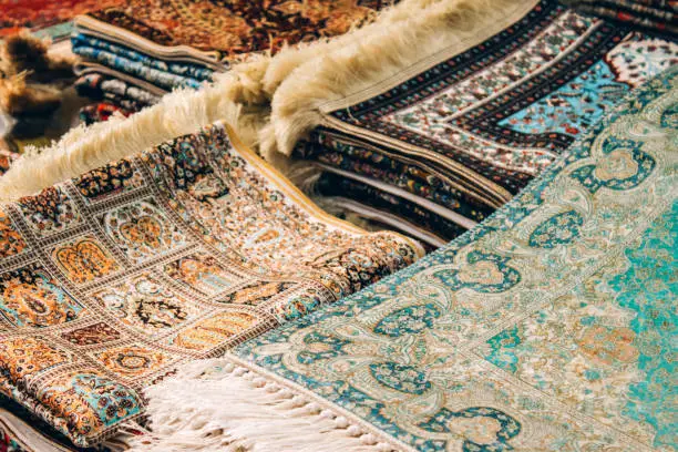 Photo of Closeup view of traditional oriental carpets and rugs as background with copy space. Multicolored ornamental carpets at carpet store. Popular touristic souvenir. Selective focus