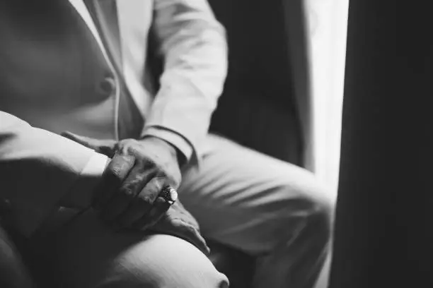 Photo of A man in a suit with a signet ring on his little finger sits by the window, close-up, black and white