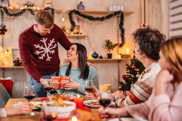 istock Man surprising girlfriend with gift at Christmas dinner with friends 1353965291