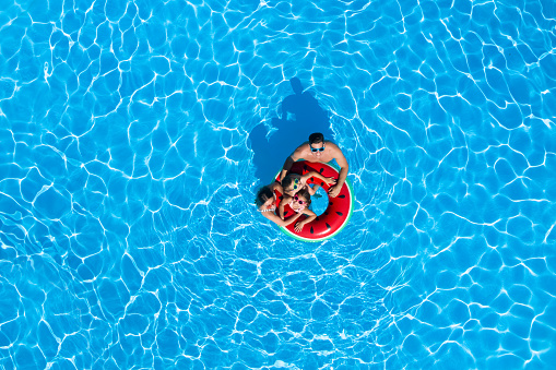 Happy family with inflatable ring in swimming pool, top view. Summer vacation