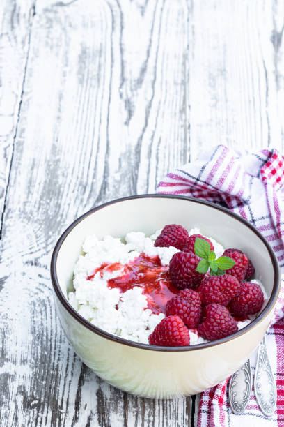 istock Cottage cheese with raspberry in ceramic bowl on white wooden table 1353965622