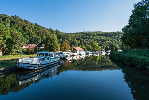Alsace, France - September 24, 2021: Tourist boats moored at the shore of a channel in the morning. Blue sky can be seen  reflecting in the calm water