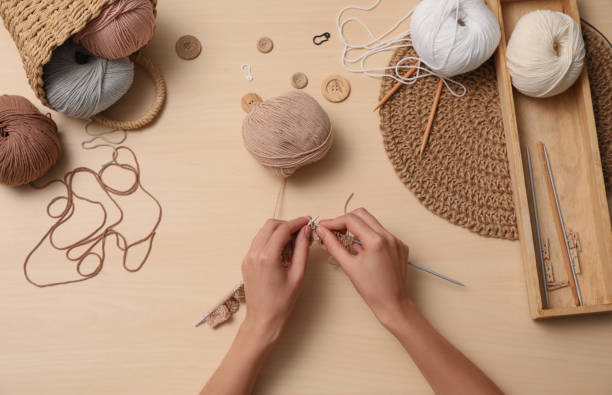 istock Woman knitting with threads at wooden table, top view. Engaging hobby 1353969923