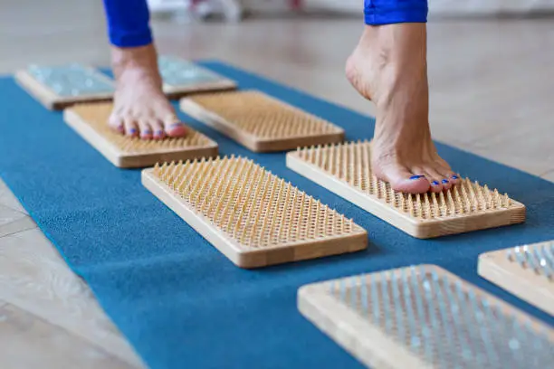 Photo of a female feet stand on a board with sharp nails over white background. Sadhu's board - practice yoga. Pain, trials, health, relaxation, cognition.