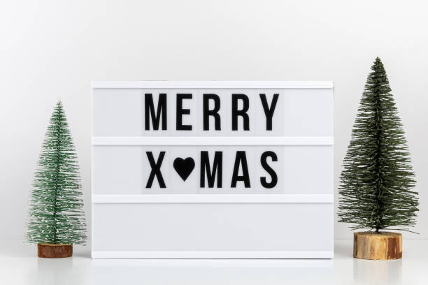 istock Two green Christmas trees and lightbox with text MERRY XMAS on white table. Minimal Christmas or New Year concept. 1353970085