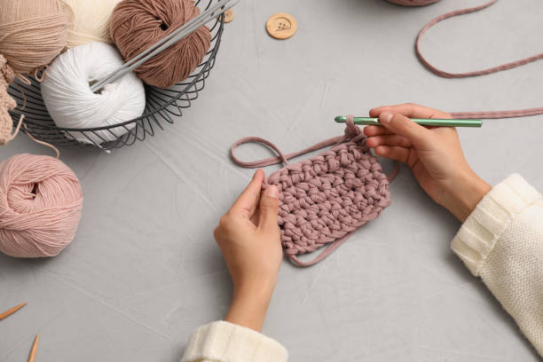 woman crocheting with threads at grey table, closeup. engaging hobby - tricotar imagens e fotografias de stock