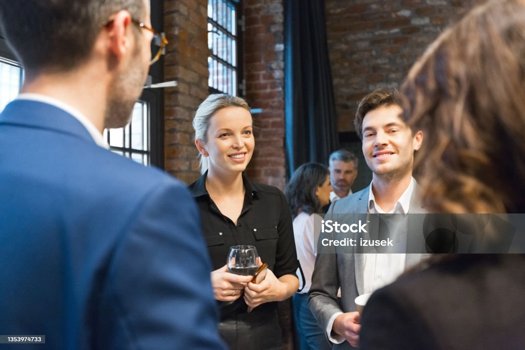 Business people during coffee break on seminar Group of mid adult entrepreneurs discussing during business seminar. Smiling businesswoman and businessmen standing in convention center in the evening. Business Stock Photo
