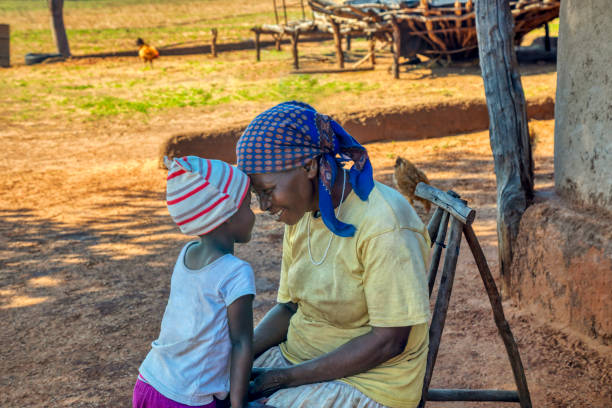 abuelita contando una historia a su nieta en el patio de un pueblo - africa child village smiling fotografías e imágenes de stock