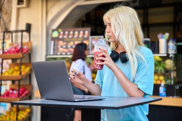 Teenage girl in fruit outdoor fruit juice bar drinking vitamin fresh juice, using laptop Teenage girl in fruit outdoor fruit juice bar drinking vitamin fresh juice, pomegranate smoothie, using laptop. Youth, summer, diet food, organic fruits, students, healthy drinks, lifestyle concept juice bar stock pictures, royalty-free photos & images