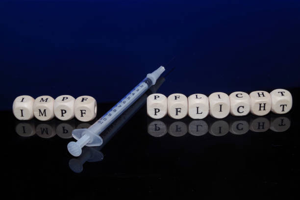 Bamberg, Germany - 16.11.2021. Conceptual picture mandatory vaccination, letter cubes, vaccination syringe, dark reflective background Bamberg, Germany - 16.11.2021. Conceptual picture mandatory vaccination, letter cubes forming the word mandatory vaccination in german language, vaccination syringe, dark reflective background mandate stock pictures, royalty-free photos & images