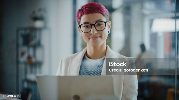 Modern Office Portrait Of Beautiful Authentic Specialist With Short Pink Hair Standing Holding Laptop Computer Looking At Camera Smiling Charmingly Working On Design Data Analysis Plan Strategy Stock Photo - Download Image Now