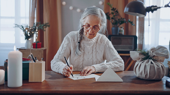 Happy senior woman writing Christmas cards indoors at home