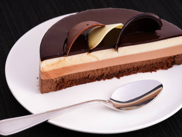 istock Half of chocolate mousse cake with spoon on a white plate. Black napkin background. 1353986706