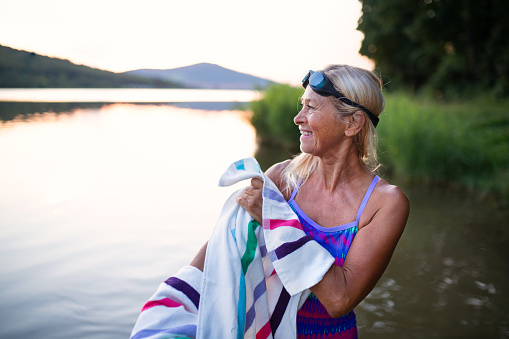 A portrait of active senior woman swimmerdrying herself with towell outdoors by lake.
