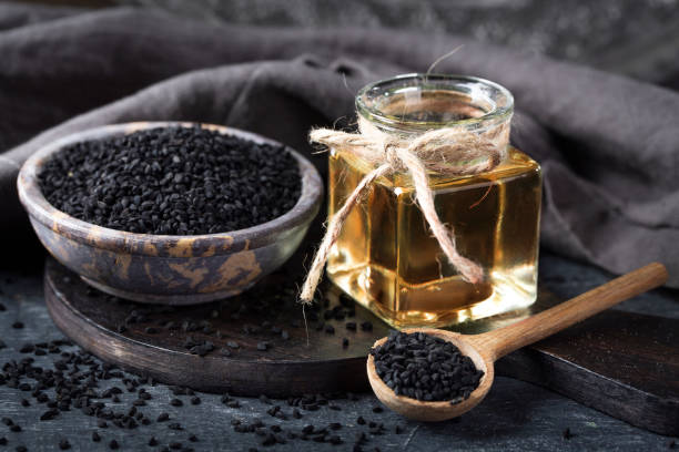 Black seeds in a bowl and oil on a black background