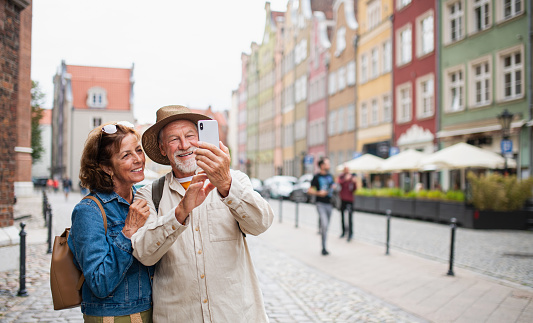 A portrait of happy senior couple tourists making selfie outdoors in historic town