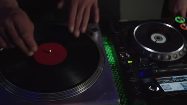 Close-up of dj hands mixing music, scratching vinyl record on turntable in nightclub