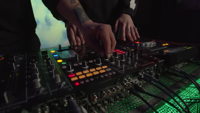 Multiethnic djs hands controlling sound mixer and cd player turntables during live set in club