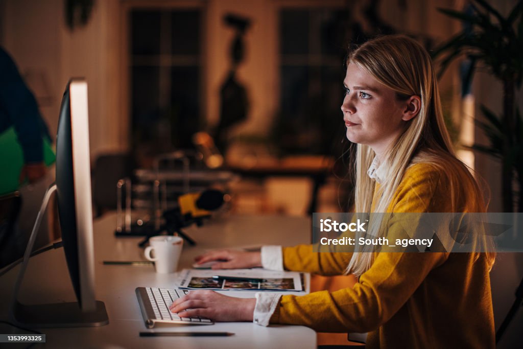 Female journalist working in office One woman, young female journalist working in news editorial office at night. Editor Stock Photo