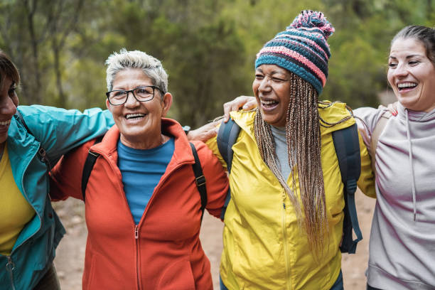 multiracial women having fun during trekking day in to the wood - focus on african female face - senior adult mountain hiking recreational pursuit imagens e fotografias de stock