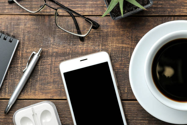 istock Smartphone white and a cup with coffee glasses and a notepad on a brown wooden table. view from above 1353995625