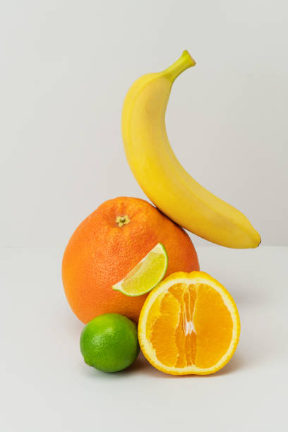 istock Fresh grapefruit, banana, cut in half orange, lime slice on light grey background. Healthy diet with vitamins. Ripe juicy fruits balanced on each other. Delicious vegan snack. Trendy still life 1353997195