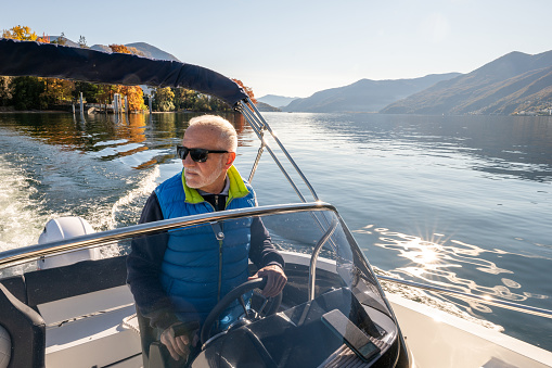 Male boat captain enjoying the lake and the mountains in Autumn.\nEarly retirement concept