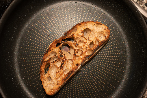 Toasting a slide of bread in a frying pan. Top view, no people, close up shot.