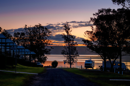 Beautiful sunset on tranquility lake with camper trailers silhouettes. Camping at holiday caravan park in Australia