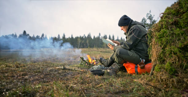 istock Man sitting near campfire and reading book in forest 1354005192