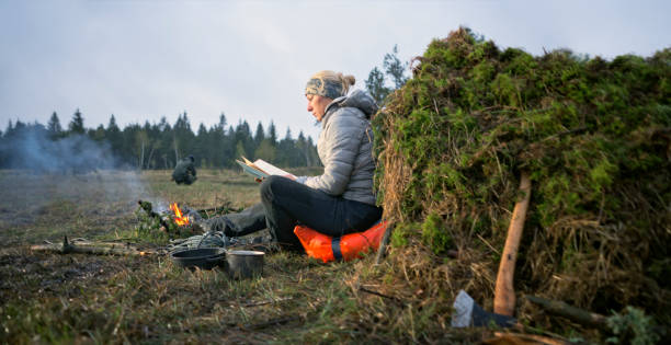 istock Woman sitting near campfire and reading book in forest 1354005202